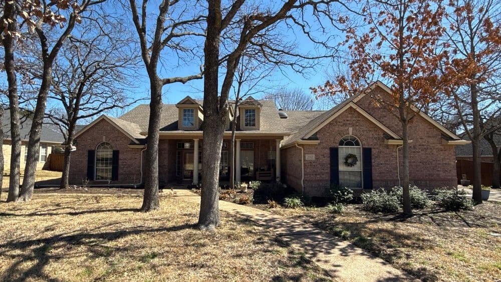 Charming brick home with large front yard and trees under a clear blue sky.