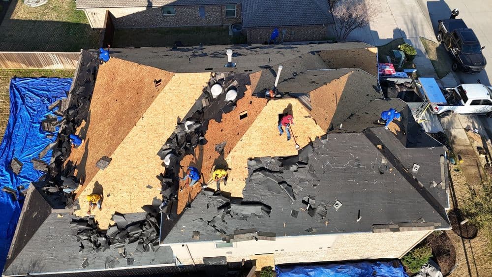 Roofing crew replacing shingles on a residential home, with materials scattered across the roof.