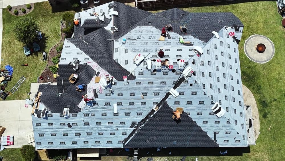 Aerial view of a residential roof installation with workers applying shingles.