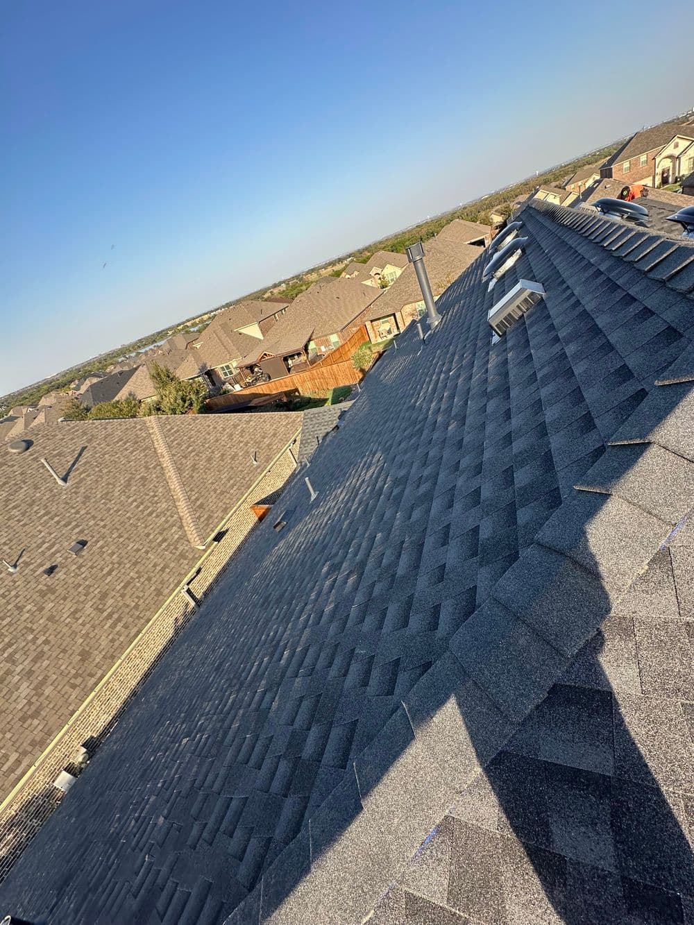 Aerial view of a gray shingle roof on a residential neighborhood under clear blue sky.