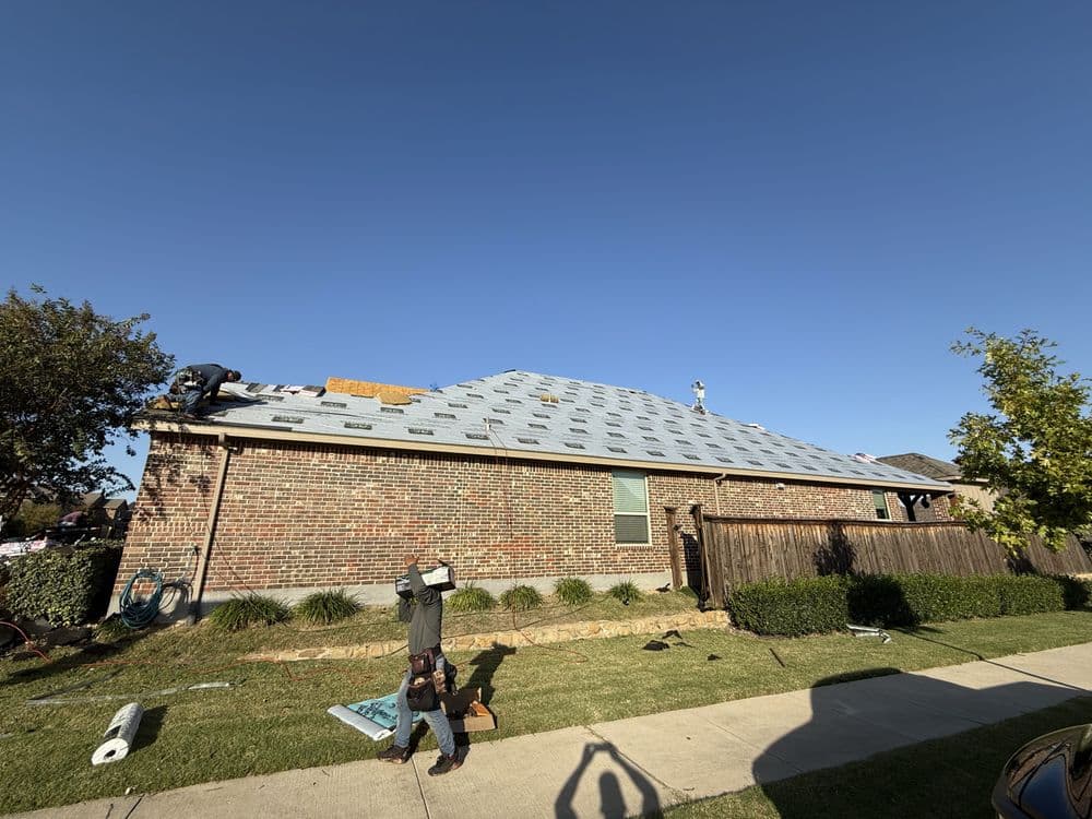 Roofing installation in progress on a residential home under a clear blue sky.