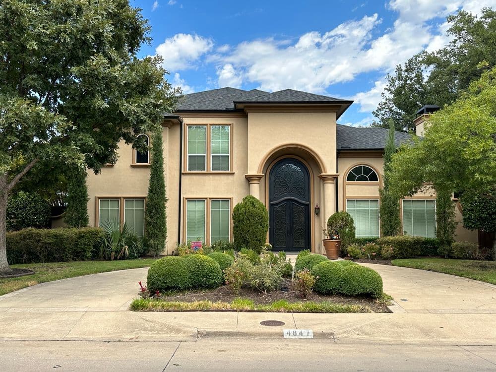 Stylish two-story house with a black front door, lush landscaping, and blue sky backdrop.