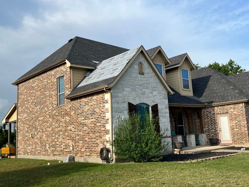 Brick and stone house exterior with green landscaping under a clear sky.