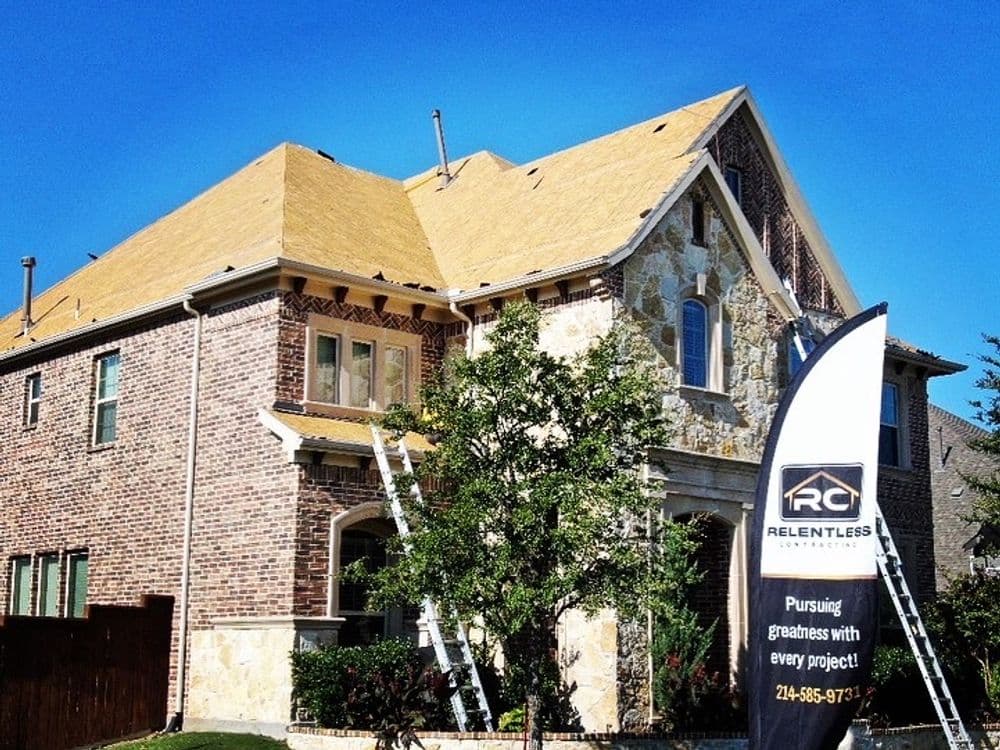 Renovated home with new roof by Relentless Contractors, featuring ladders and a promotional sign.