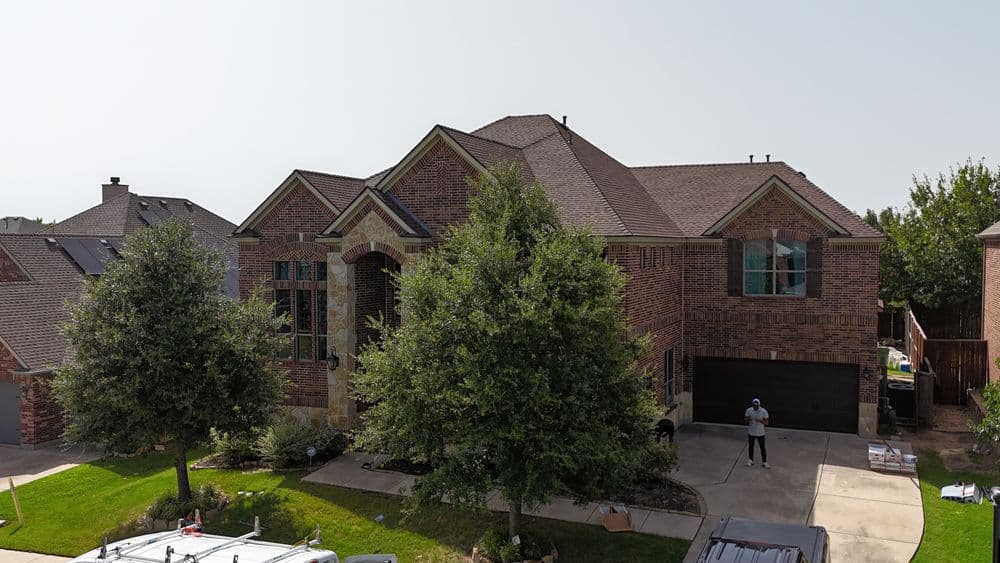 Modern brick house with a landscaped yard and two trees in front, featuring a driveway and garage.
