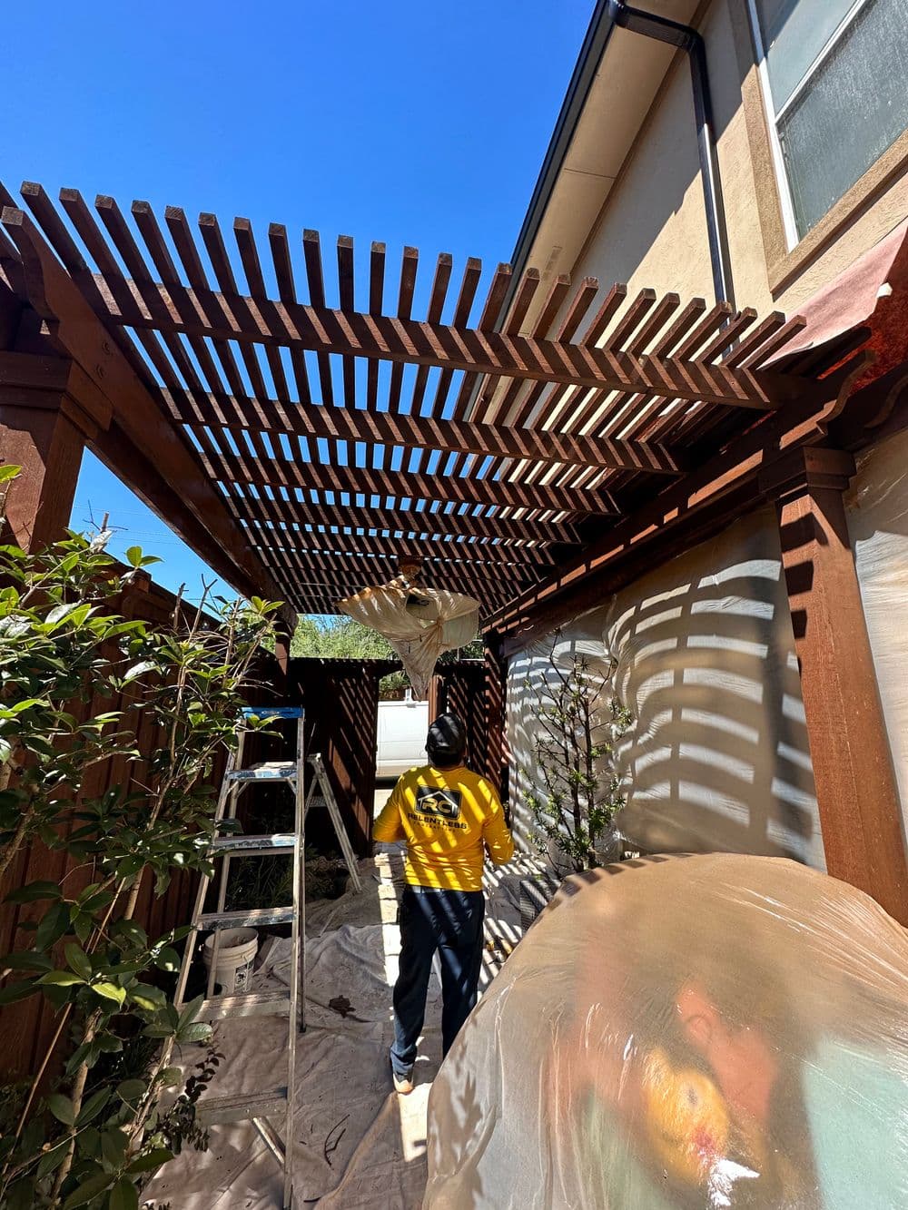 Person painting a wooden pergola with a clear blue sky in the background.