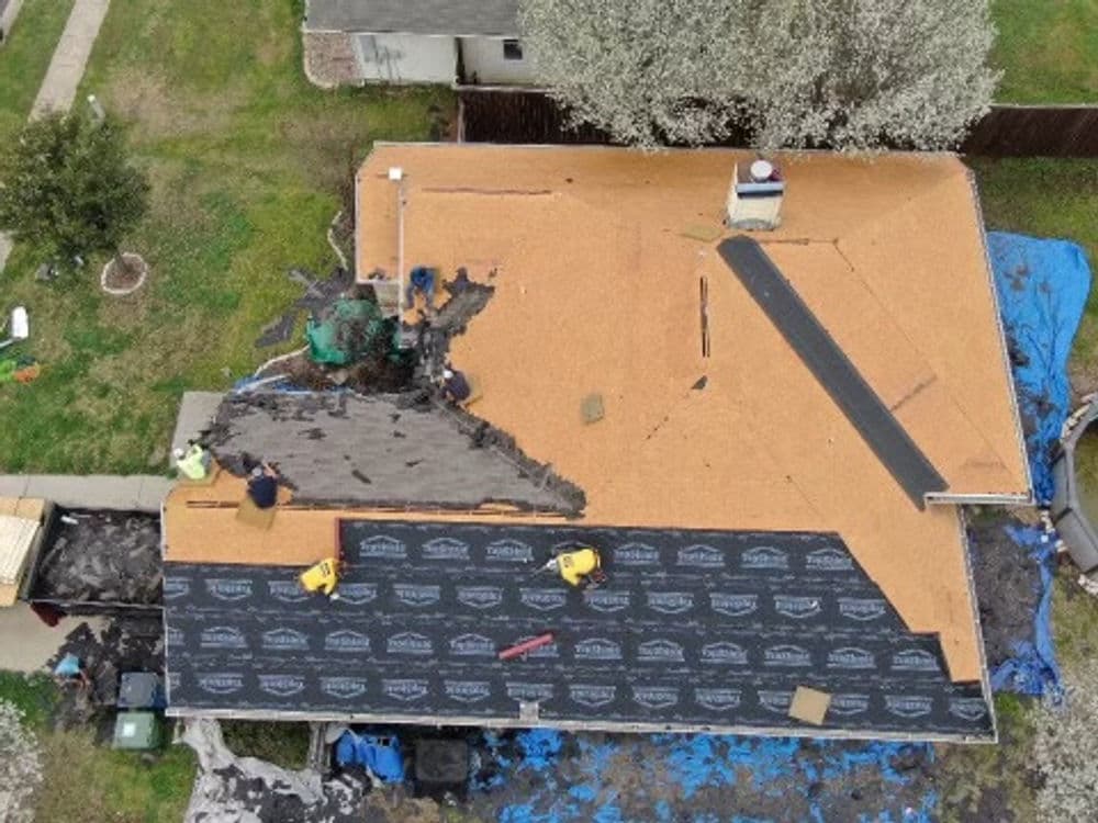 Aerial view of a home undergoing roof replacement with workers and materials on-site.