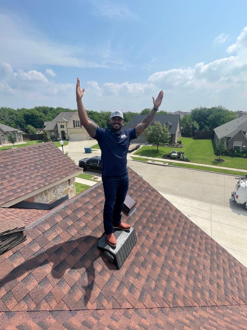 Man standing on a roof, arms raised in celebration, with suburban homes in the background.