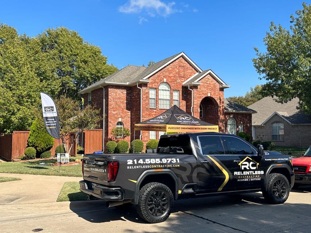 Truck with Relentless Contracting branding parked in front of a brick house with a tent and banner.