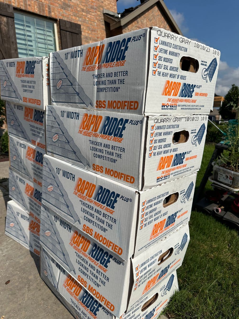 Stacked boxes of Rapid Ridge roofing material in Quarry Gray, labeled SBS Modified, for construction use.