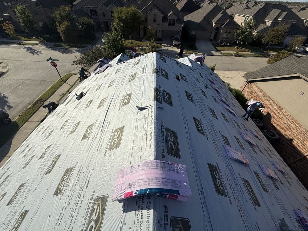 Workers installing roofing material on a steep residential roof under clear blue skies.