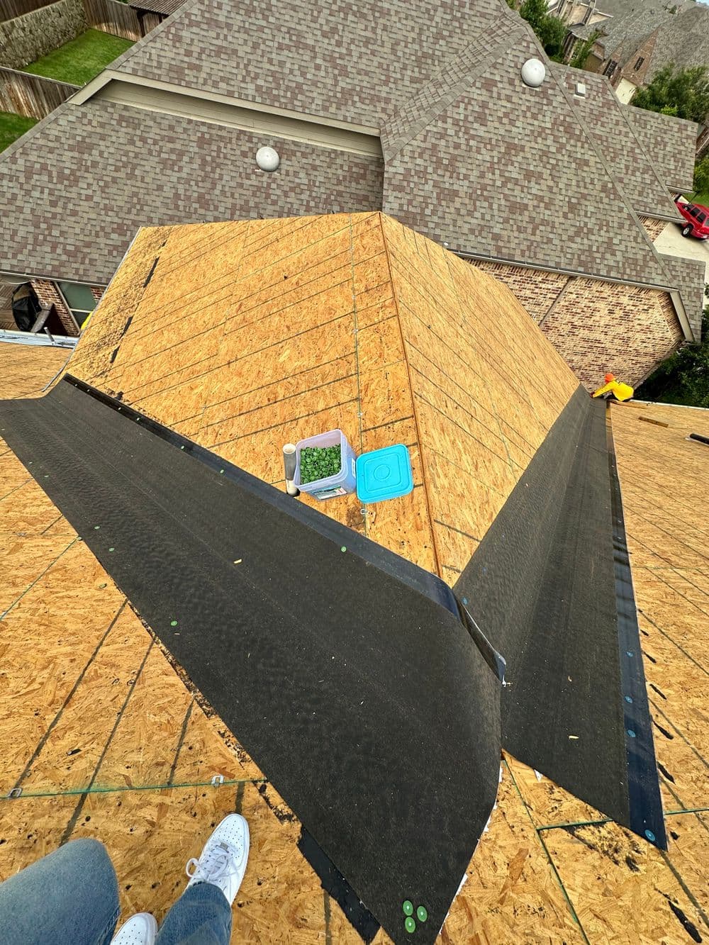Aerial view of a roof under renovation with plywood and roofing felt installed.