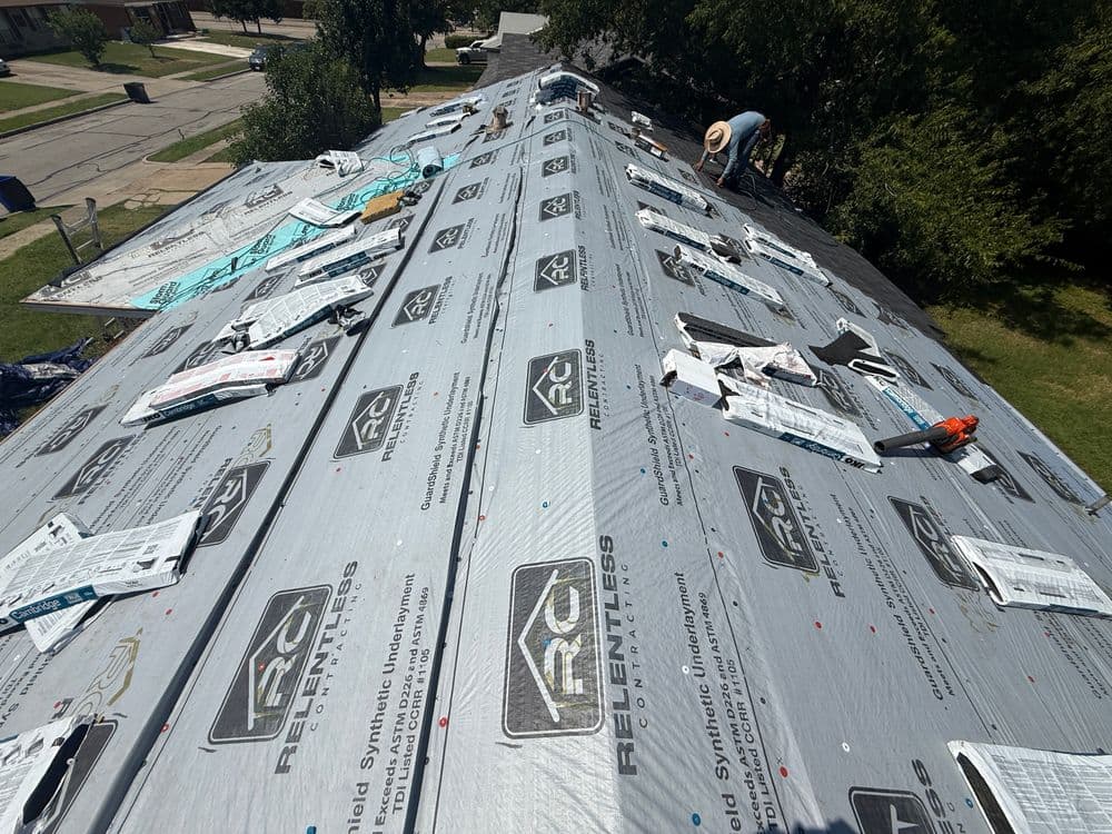 Roof installation in progress with synthetic underlayment and tools visible.
