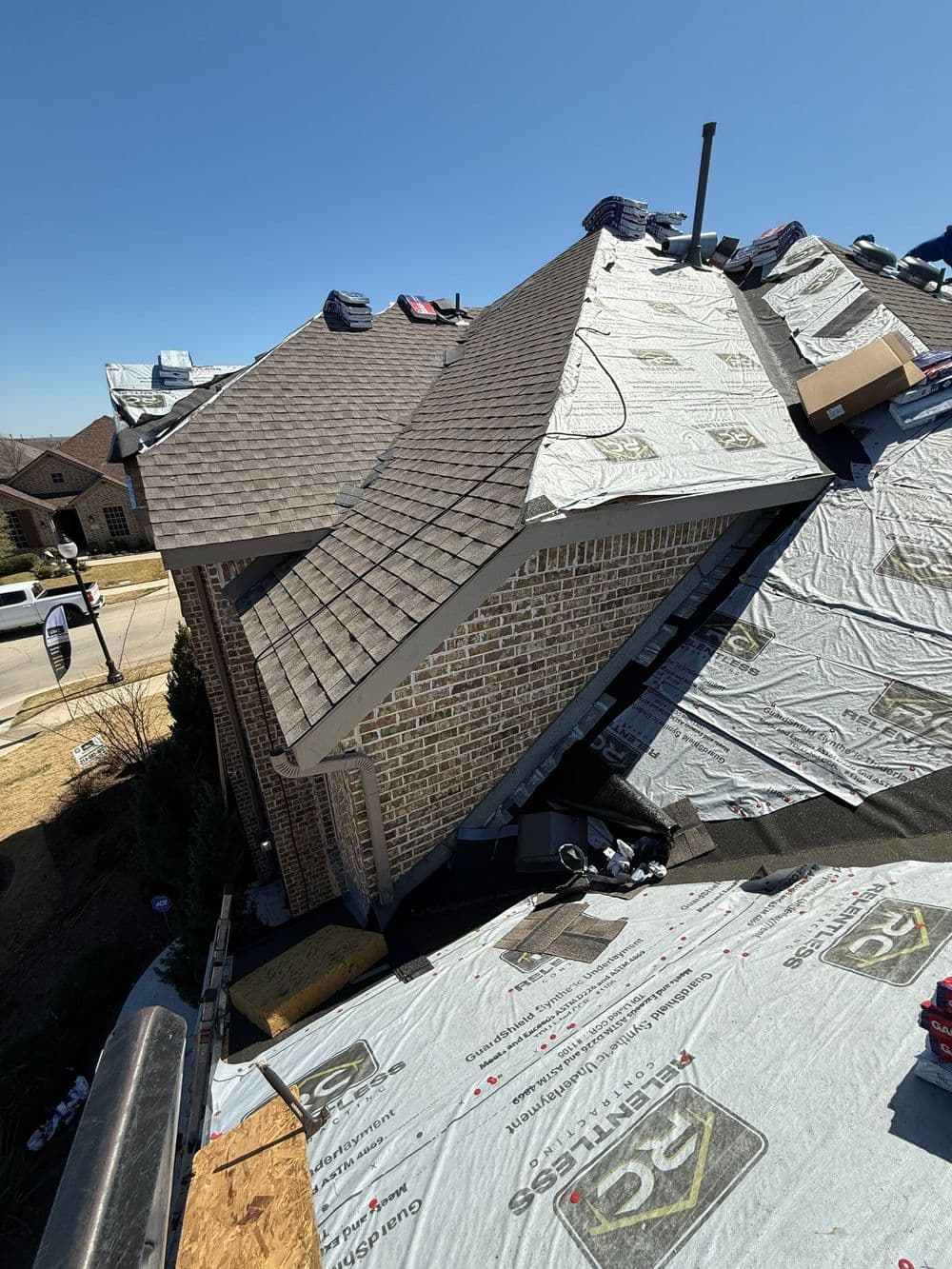 Roofing project in progress with tarp and materials on a residential home. Clear blue sky.