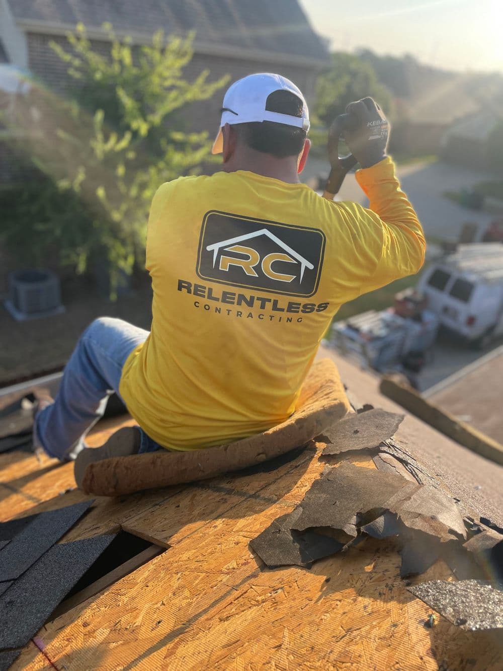 Roofer in yellow shirt working on a residential roof, removing shingles during repairs.