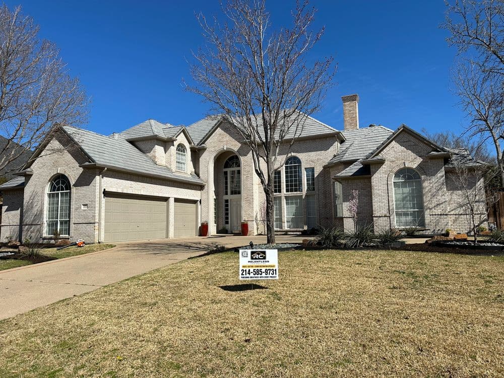 Elegant brick house with a two-car garage and well-maintained lawn, showcasing clear blue skies.