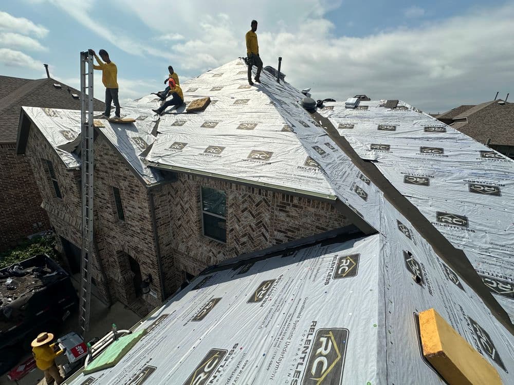 Roofing crew installing new shingles on a residential home with a clear sky above.