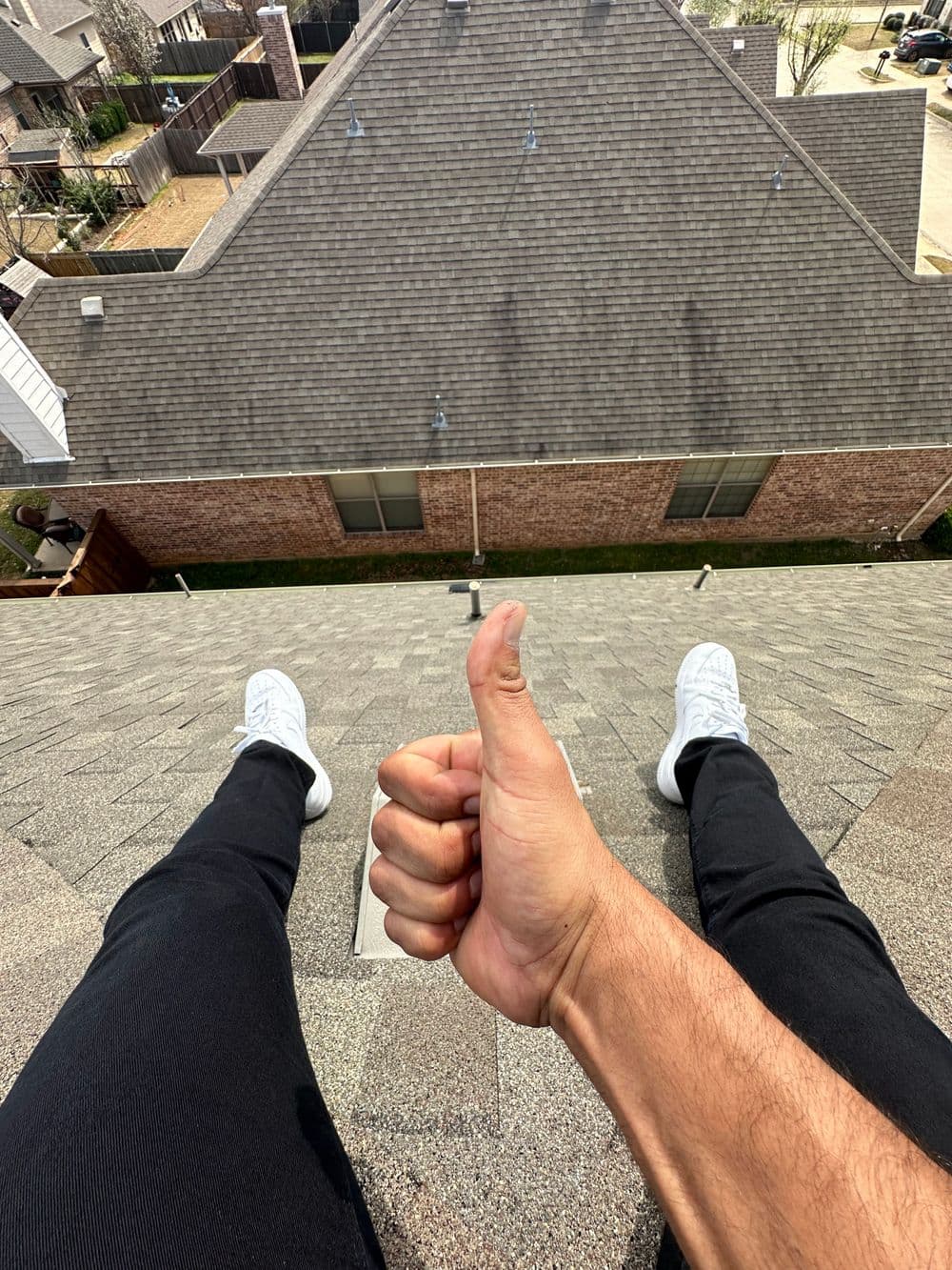 Person sitting on a roof giving a thumbs up, wearing white shoes and black pants.