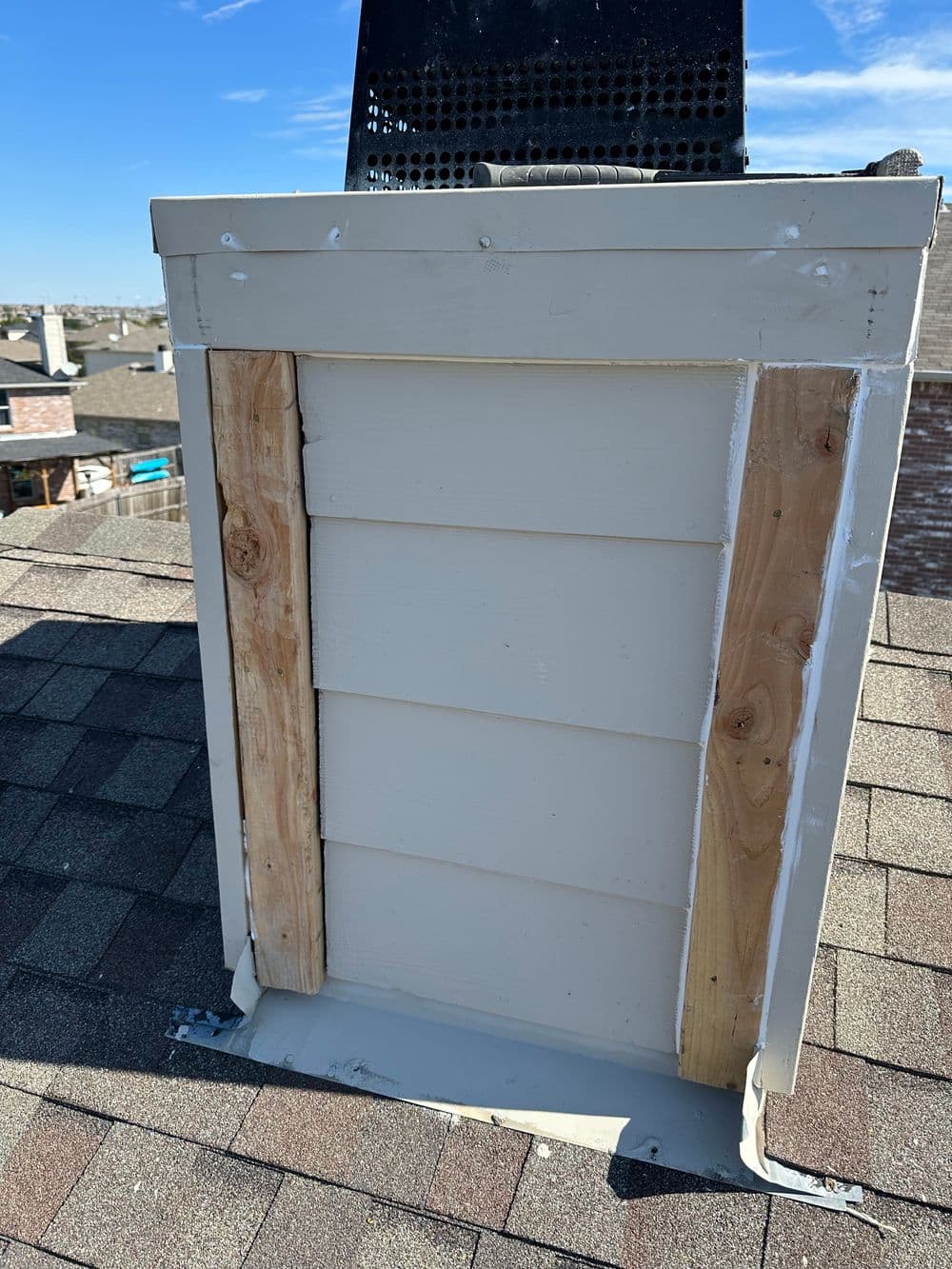 Roof chimney with wooden framing and clear blue sky in the background, showcasing home repair.