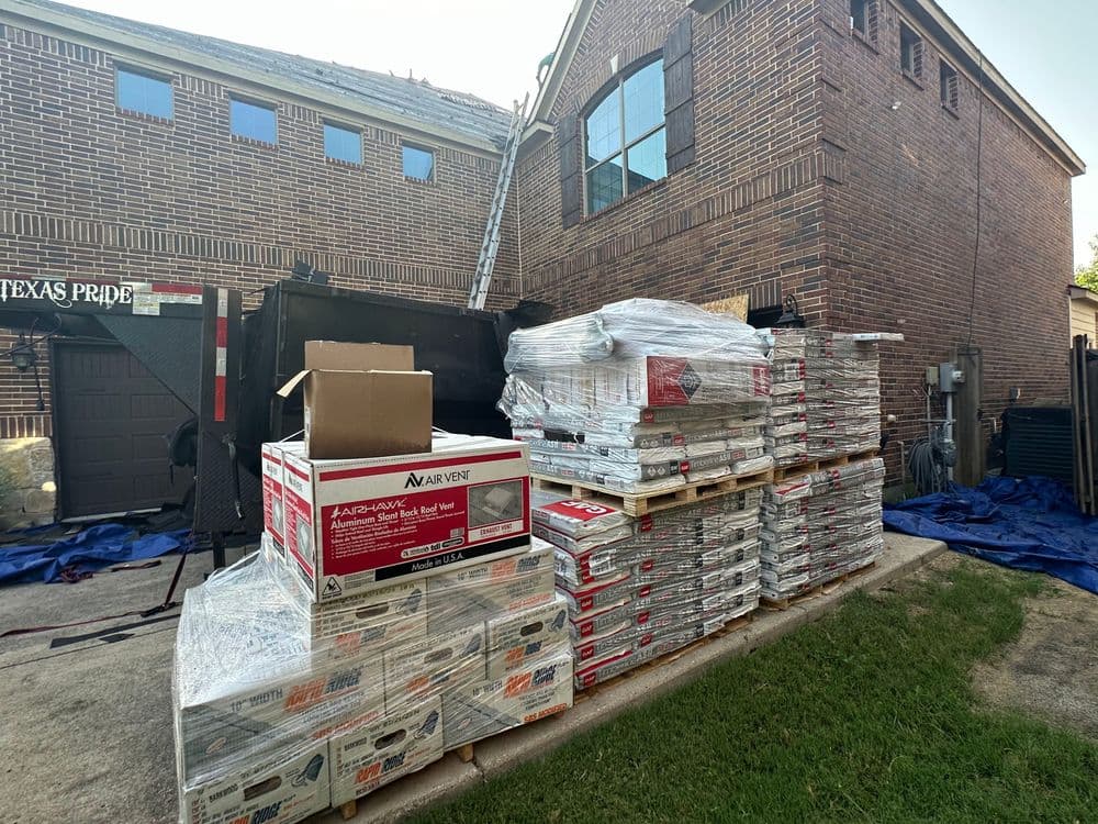 Stacked building materials beside a house, with ladders and construction equipment visible.