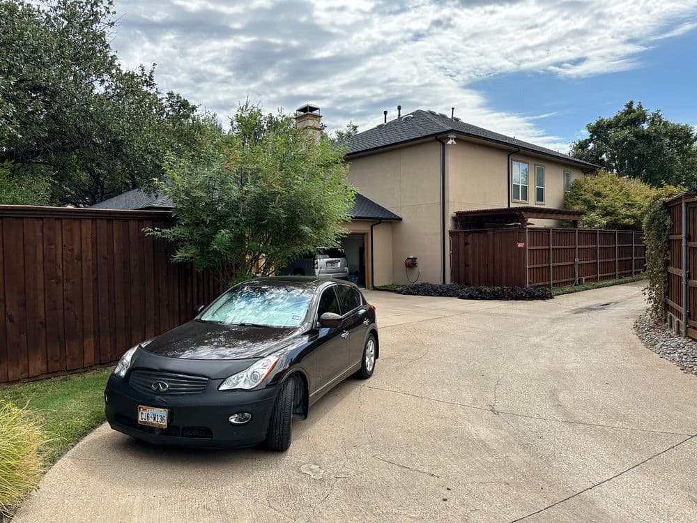 Black SUV parked in a driveway beside a modern home with wooden fencing and blue sky.