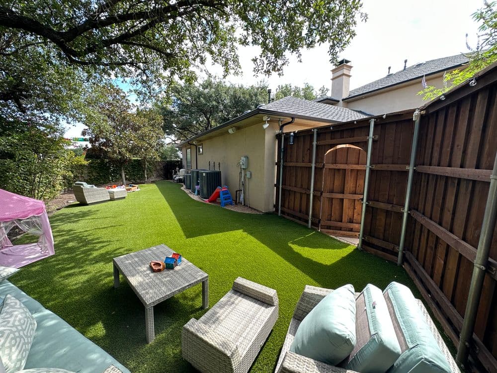 Backyard with artificial grass, outdoor seating, and play equipment for children.