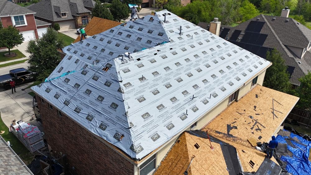 Roofing installation in progress with workers applying underlayment on a residential home.
