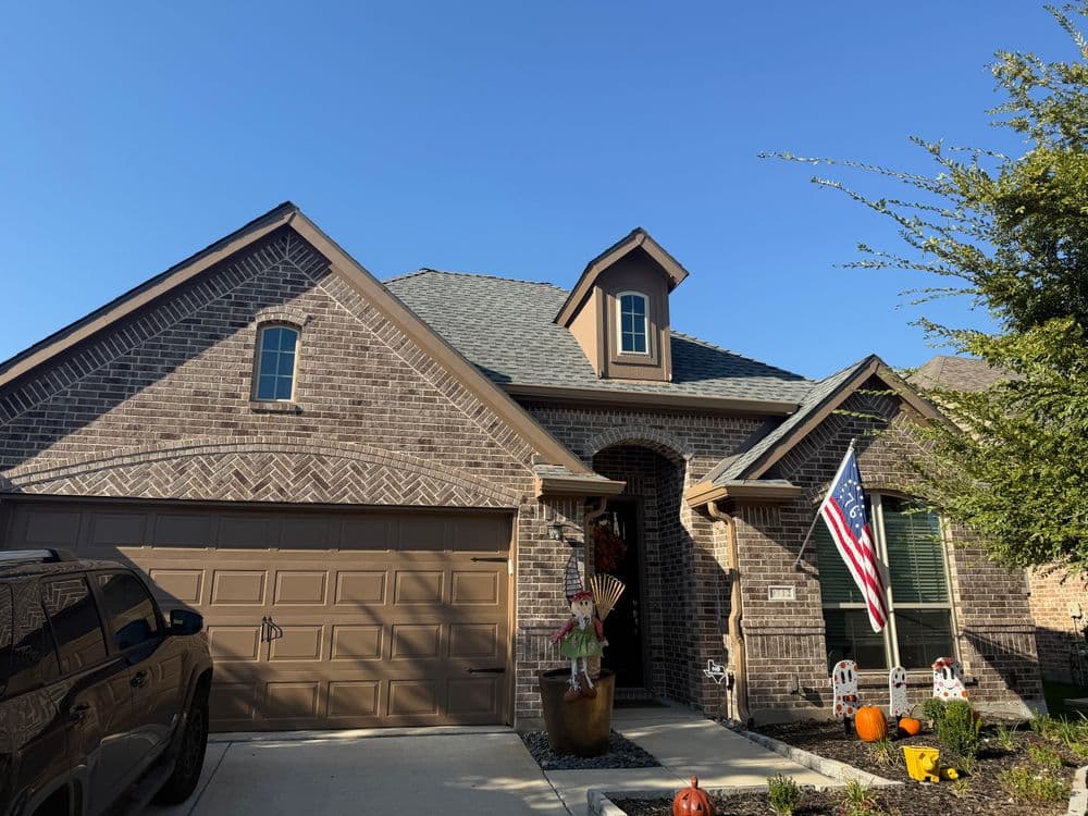 Brick house with American flag, festive fall decorations, and clear blue sky.