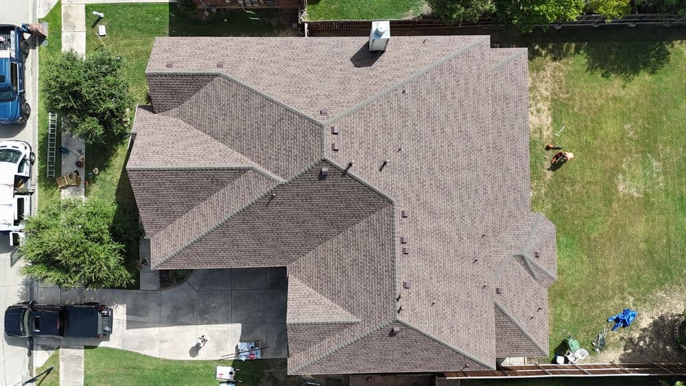 Aerial view of a residential home with a brown shingle roof and surrounding yard.