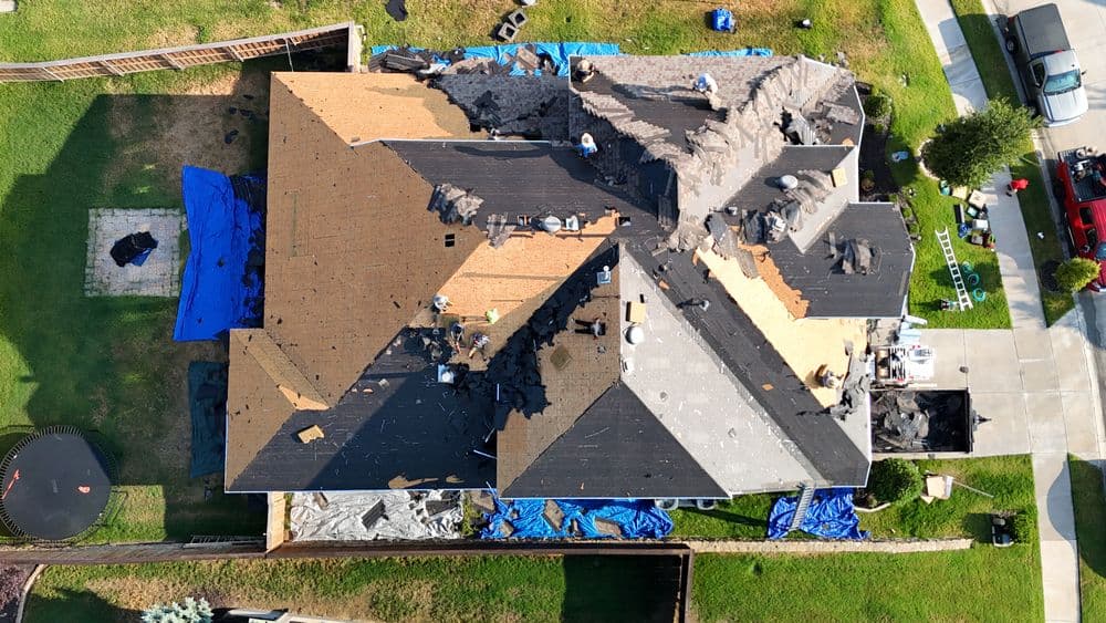 Aerial view of a house with roof renovation, featuring workers, tarps, and roofing materials.