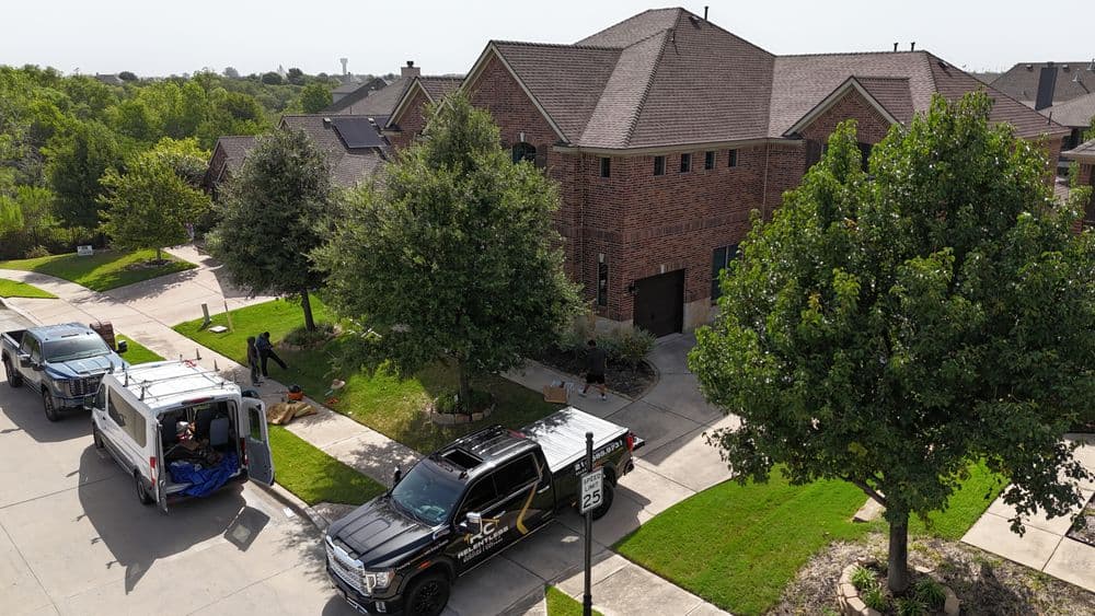Aerial view of a suburban home with vehicles and landscaping activities on a sunny day.